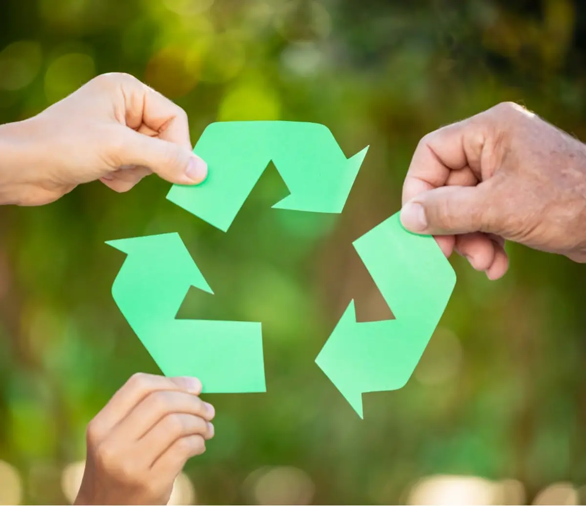 Three hands holding pieces of a green recycling symbol