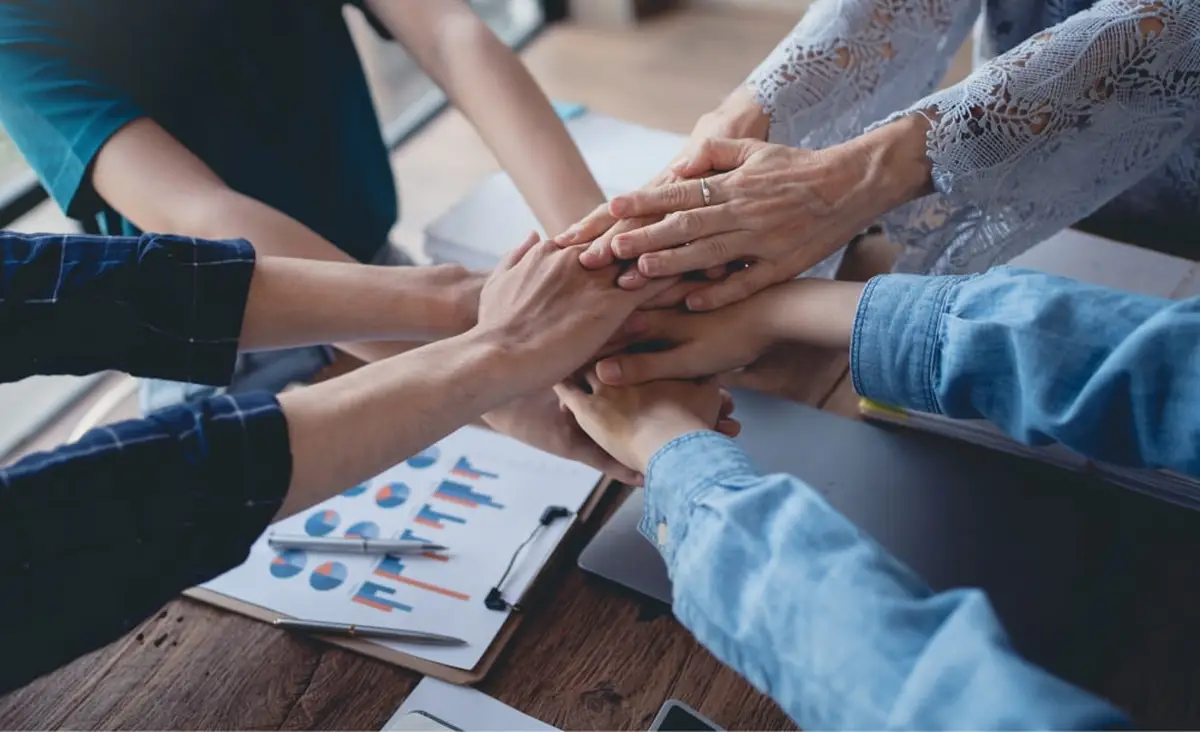 Team stacking hands over a desk with business charts